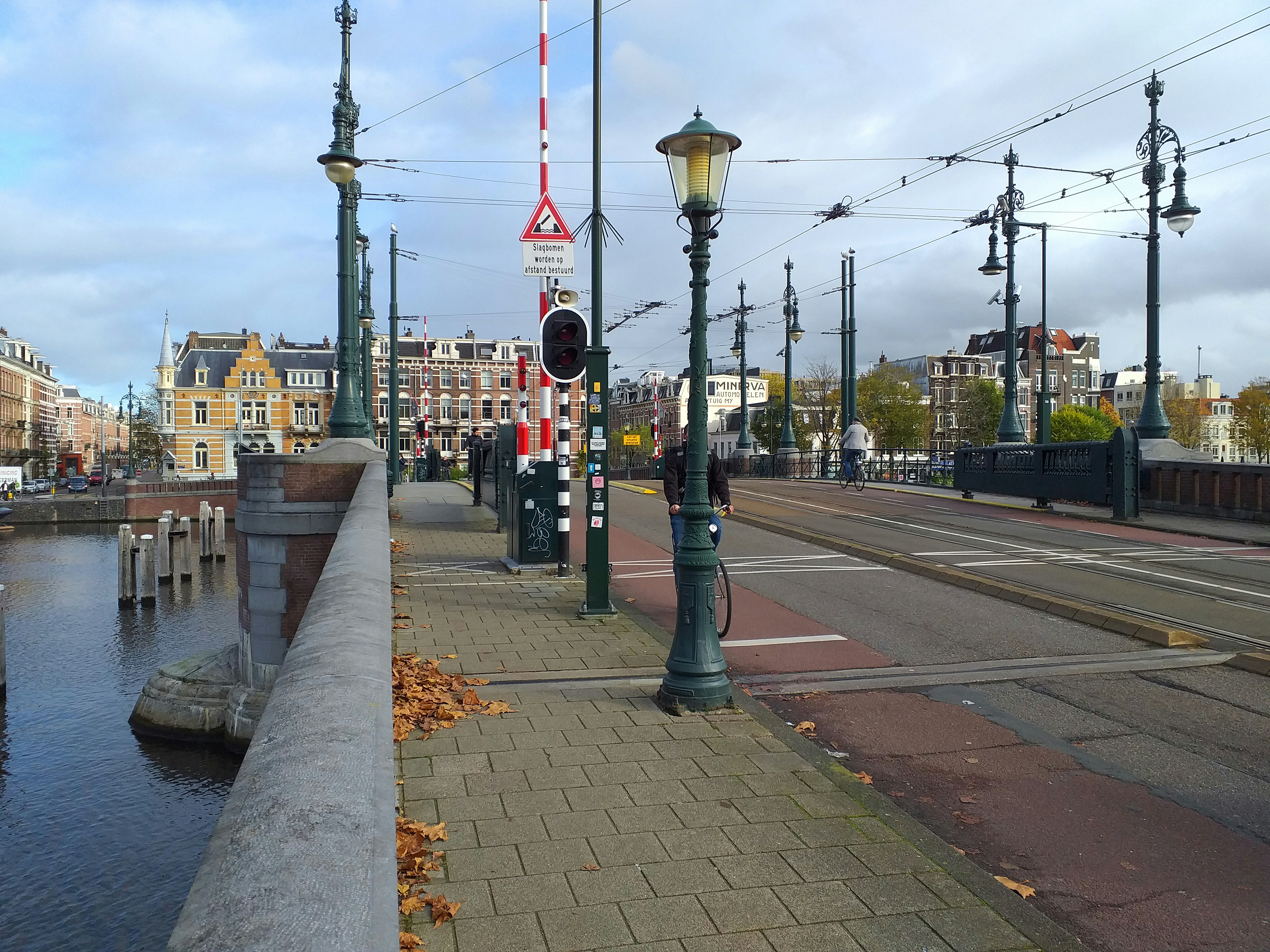 Street view over the stone wide bridge over the river Amstel in Amsterdam city with street lights on both sides, under a grey blue shade sky in Fall. A street view with brick house facades in the background. Free street photography of Amsterdam city and river by Fons Heijnsbroek, The Netherlands, November 2021 // Foto van de Nieuwe Amstelbrug bij de Ceintuurbaan - hier over de Amstel in Amsterdam, met trambaan en straatlantaarn, en de gevels van de Weesperzijde - gratis downloaden. Foto, Fons Heijnsbroek - fotografie van bruggen in Nederland, hoge resolutie en rechtenvrije afbeeldingen, CCO