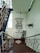 A stairwell features motivational text on the wall reading 'Success is the ability to go from one failure to another with no loss of enthusiasm - Winston Churchill'. The space is well-lit with natural light coming from a window. Several potted plants are placed around, enhancing the calm atmosphere. The staircase is adorned with metal railings.