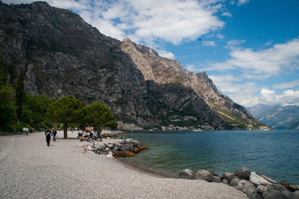 a body of water with people walking along it and mountains in the background