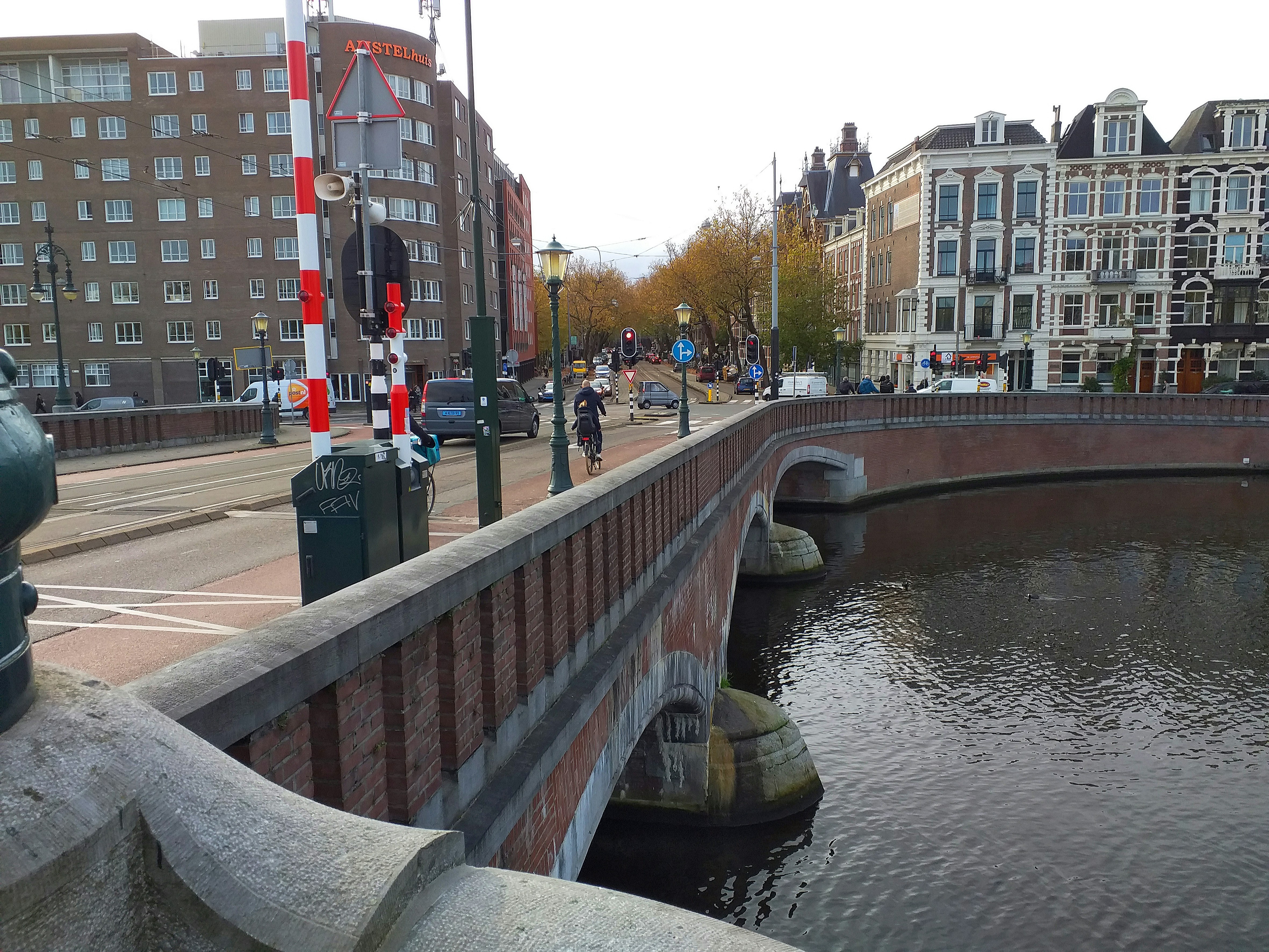 Street view over the bridge Nieuwe Amstelbrug, over the water of river Amstel under a light grey sky above Amsterdan city. The bridge has many stone ornaments and decorations and a brick railing, all in the architecture style of Amsterdam School. Free city photography of Fons Heijnsbroek, November 2021; The Netherlands // Foto van de Nieuwe Amstelbrug aan de Ceintuurbaan, over de Amstel in Amsterdam, gebouwd in de architectuur van de Amsterdamse School stijl - gratis downloaden. Foto, Fons Heijnsbroek - fotografie van gebouwen in Nederland, hoge resolutie afbeeldingen.