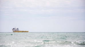 A dark yellow sea with a large shipping container vessel cutting through the waves under a moody sky.