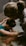 Two people appear to be engaged in a soothing, intimate moment, possibly involving support or care. One person is in a tub of water, with their head resting on their arms, while the other person leans over from outside the tub, gently touching and comforting them.