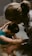 Two people appear to be engaged in a soothing, intimate moment, possibly involving support or care. One person is in a tub of water, with their head resting on their arms, while the other person leans over from outside the tub, gently touching and comforting them.