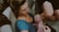 A woman holds a newborn baby close to her chest while sitting in a bathtub. The baby is freshly born, with a visible amount of vernix on the skin. The scene suggests an intimate and tender moment between the mother and child during or right after a water birth.
