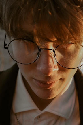 Side profile of a young woman trying on round, gold-framed eyewear.