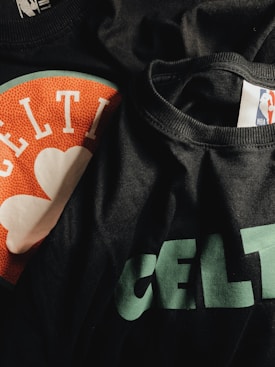 A close-up of black fabric featuring printed designs, including the text 'Celtics' and an NBA logo, as well as elements resembling a basketball texture in orange and white.