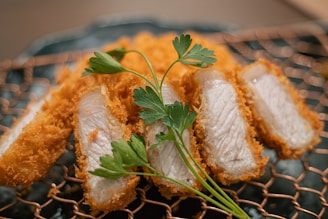 Pieces of breaded and fried meat, possibly pork, are arranged attractively on a wire cooling rack. The slices are garnished with fresh parsley, which adds a bright touch of green against the golden brown of the crust.