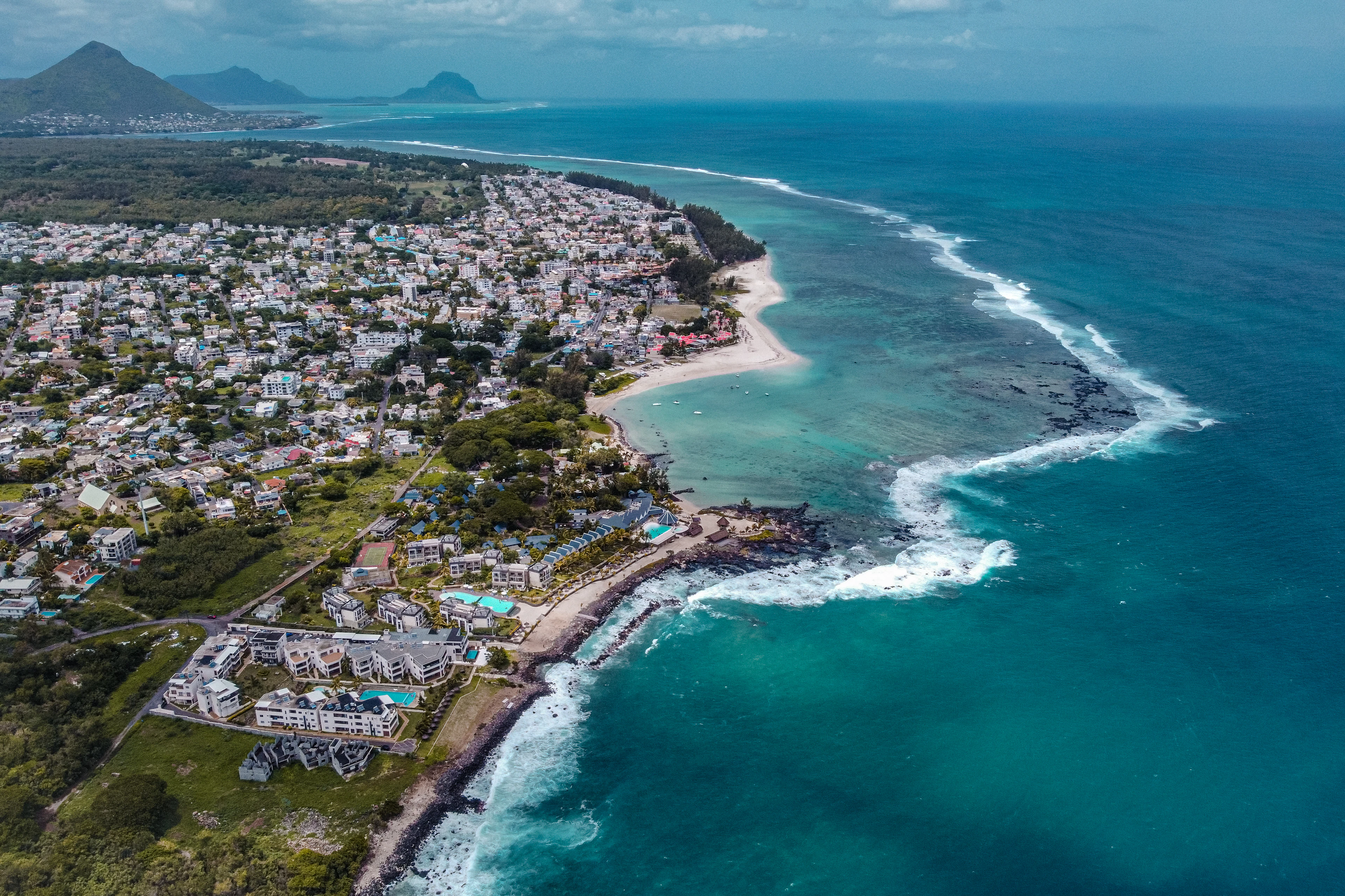 An aerial view of a curving coastline where a turquoise reef meets a beachfront resort town.