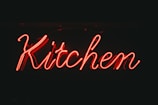 Bright red neon sign displaying the word 'Kitchen' against a dark background.