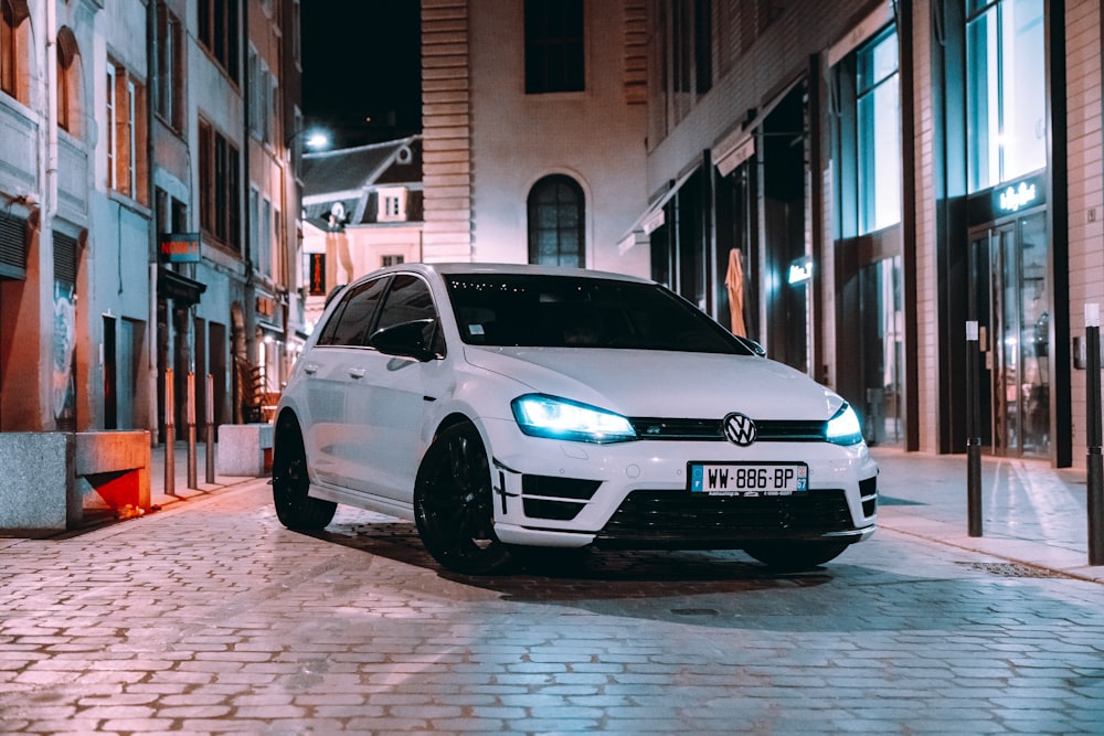 a white car parked on a brick road between buildings