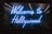 A vibrant neon sign displays the words 'Welcome to Hollywood' in bright blue light, set against a backdrop of lush green foliage, creating a striking contrast that draws attention.