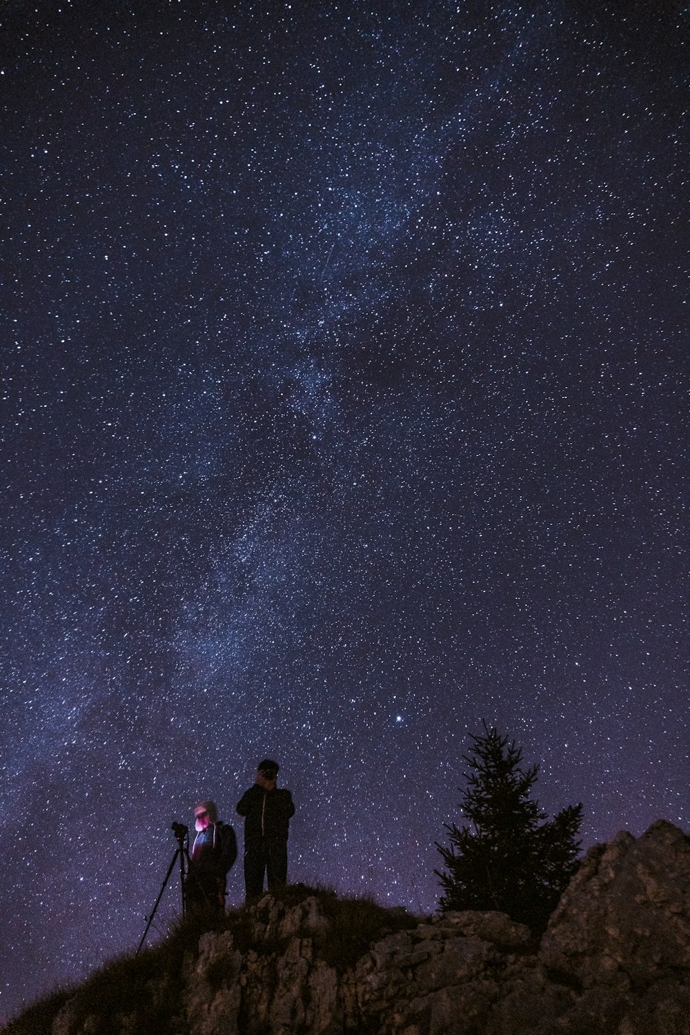 a man and woman standing on a rocky hill with a starry sky above