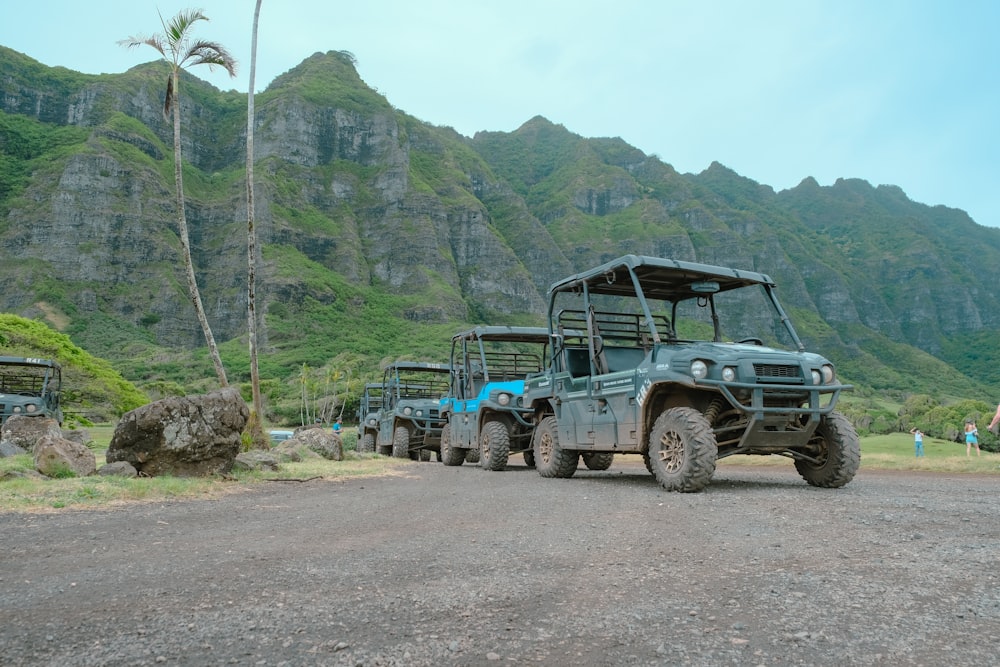 a couple of military vehicles parked on a dirt road by a mountain