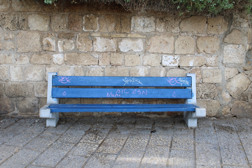 a blue bench sits in front of a stone wall