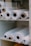 Several large rolls of white fabric are neatly arranged on white shelves. The rolls have visible cardboard tubes at their centers and vary slightly in texture. They appear organized and ready for use, suggesting a warehouse or fabric store setting.