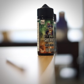 A bottle of flavored vape liquid with a pirate-themed label sits on the edge of a table in a softly blurred background.