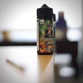 A bottle of flavored vape liquid with a pirate-themed label sits on the edge of a table in a softly blurred background.