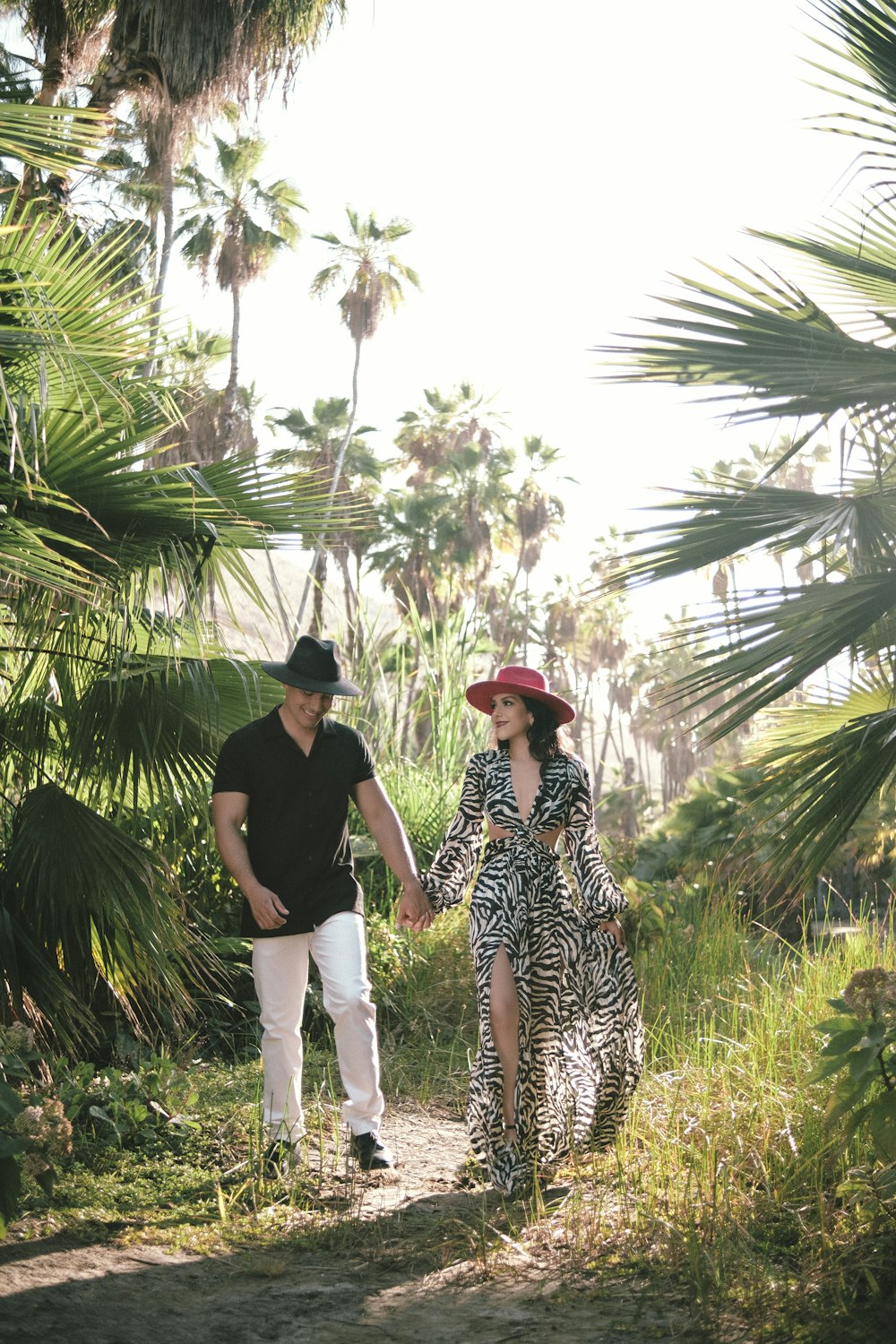 a man and woman walking on a path between palm trees