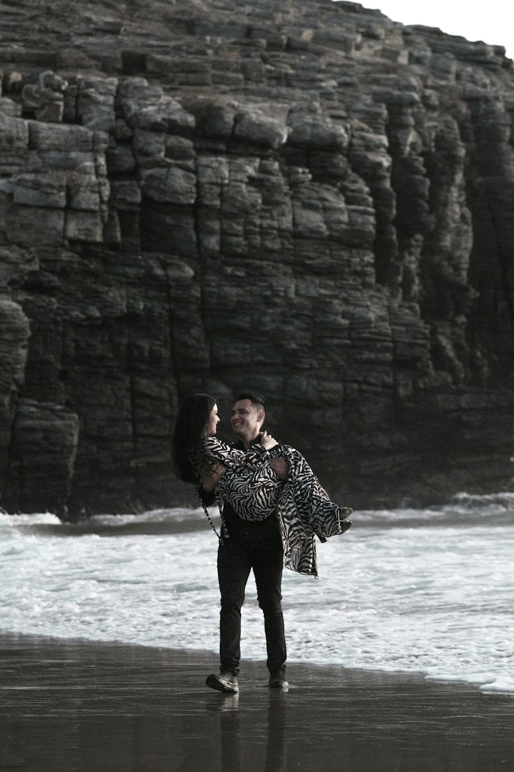 a man and woman hugging on a beach by a cliff