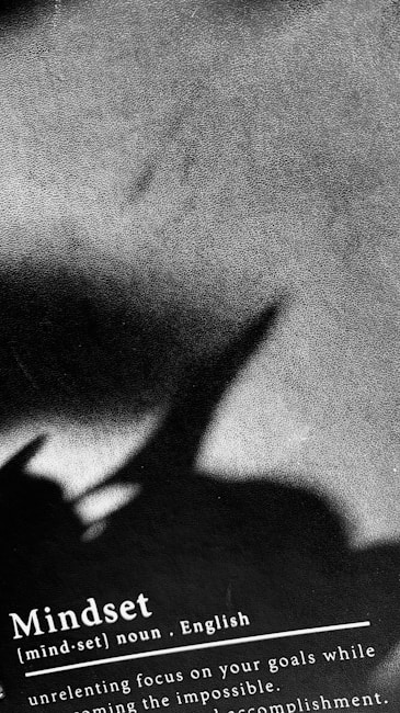 A textured surface in grayscale with the shadow of a plant or object creating an abstract pattern. The bottom of the image contains text defining the word 