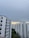 A cluster of high-rise residential buildings with white facades and pink accents under an overcast sky. There is a patch of greenery visible in the lower part of the image.