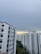 A cluster of high-rise residential buildings with white facades and pink accents under an overcast sky. There is a patch of greenery visible in the lower part of the image.