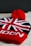 A close-up of a knitted winter hat featuring the design of the Union Jack, with red, white, and black colors. The hat has a red pom-pom on top and the word 'London' knitted near the brim. The background is a neutral, dark color, which contrasts with the bright colors of the hat.