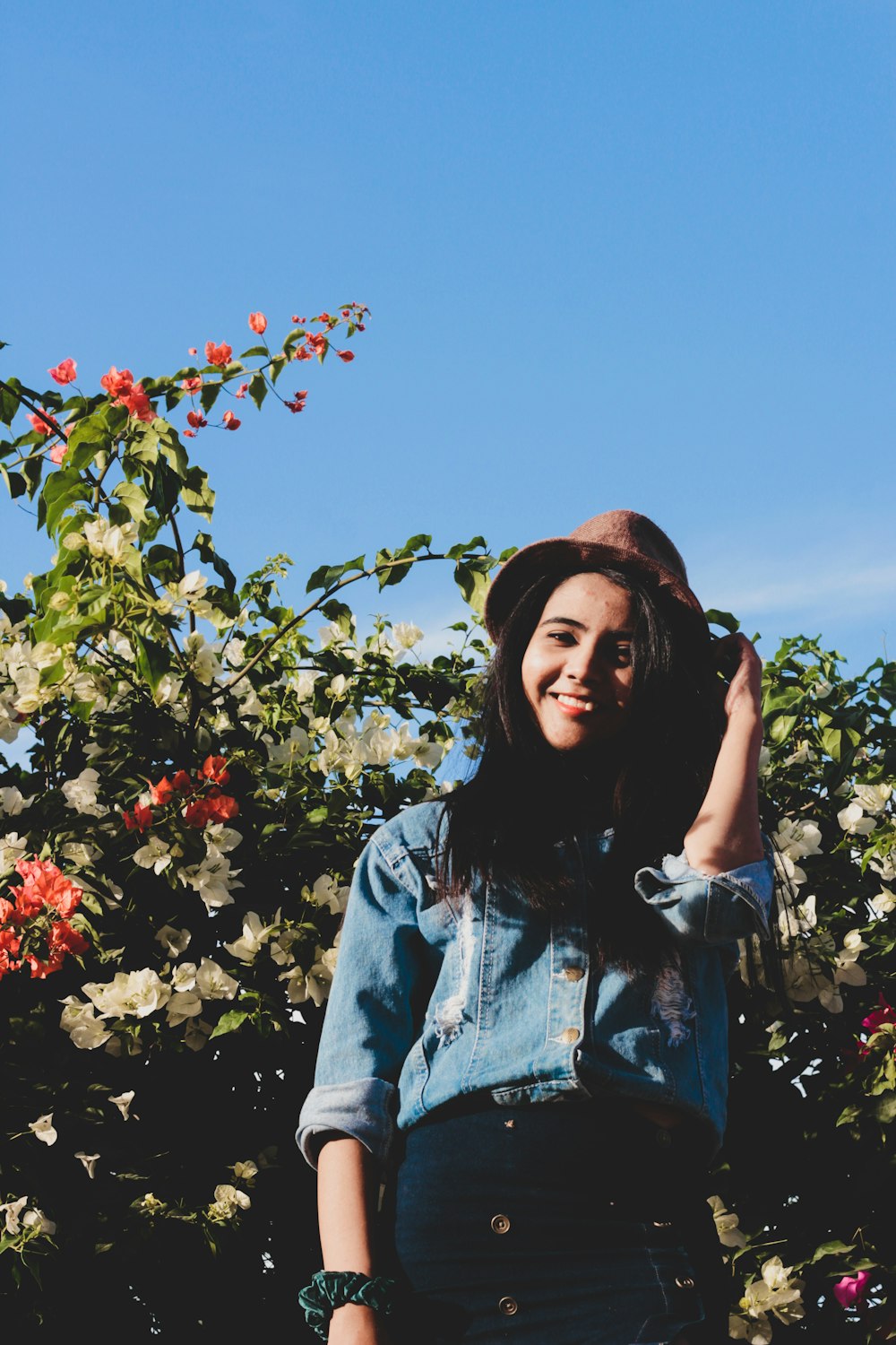 a woman standing in front of a bush with flowers