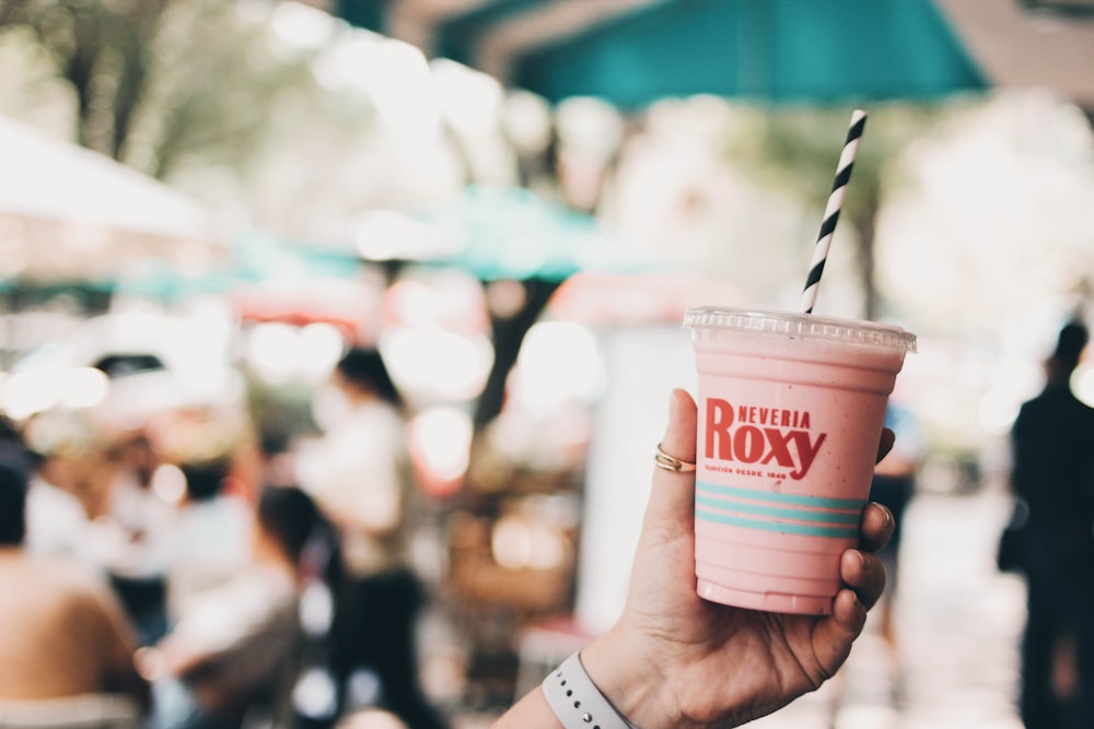 a hand holding a plastic cup with a straw