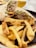 A plate of crispy golden-brown fries is served alongside a wrap filled with shredded meat, lettuce, and possibly other vegetables. The meal is arranged on a dark plate with a bowl containing a yellow sauce in the background.