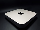 A sleek, minimalist electronic device with rounded edges, featuring a prominent logo on the top surface. The device rests on a dark surface, giving it a modern and sophisticated appearance.