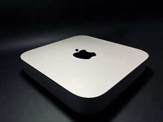 A sleek, minimalist electronic device with rounded edges, featuring a prominent logo on the top surface. The device rests on a dark surface, giving it a modern and sophisticated appearance.