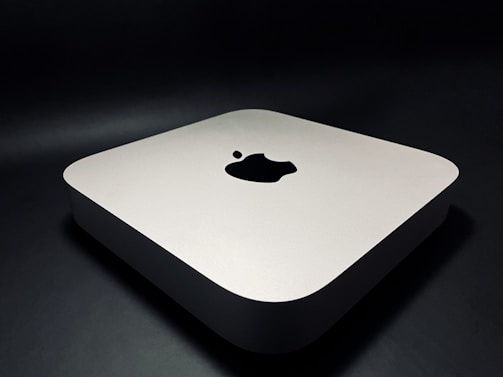 A sleek, minimalist electronic device with rounded edges, featuring a prominent logo on the top surface. The device rests on a dark surface, giving it a modern and sophisticated appearance.