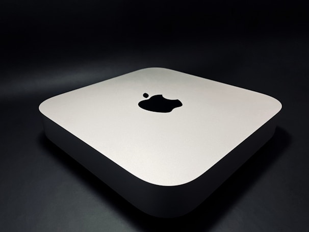 A sleek, minimalist electronic device with rounded edges, featuring a prominent logo on the top surface. The device rests on a dark surface, giving it a modern and sophisticated appearance.