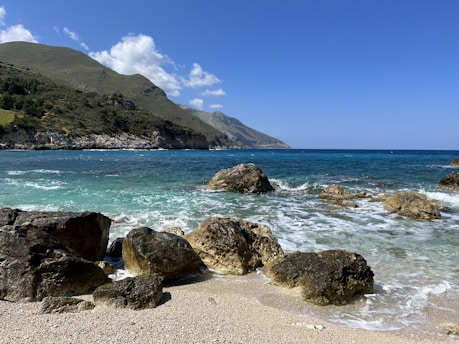 a rocky beach with a body of water and mountains in the background