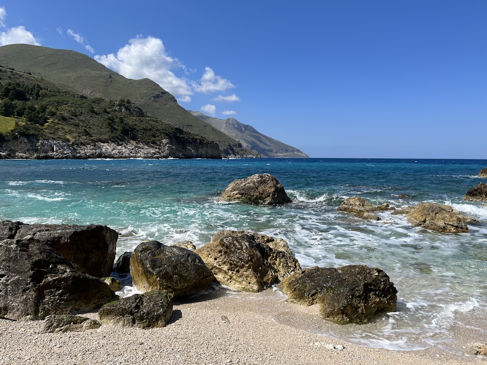 a rocky beach with a body of water and mountains in the background