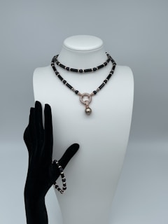 A mannequin bust wearing a black and gold beaded necklace with a large round pendant, paired with a matching beaded bracelet on a black velvet glove.