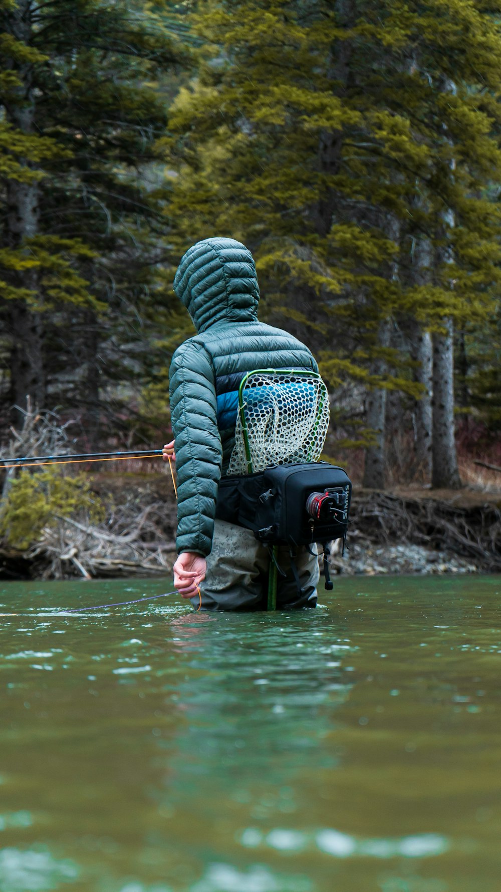 a person in a raincoat standing in water with a backpack