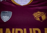 A maroon sports jersey prominently features two logos. On the left side is a silver shield with the text 'Scotiabank CONCACAF League Champions 2021'. On the right is a gold and maroon crest with 'COMUNICACIONES' printed.