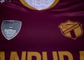 A maroon sports jersey prominently features two logos. On the left side is a silver shield with the text 'Scotiabank CONCACAF League Champions 2021'. On the right is a gold and maroon crest with 'COMUNICACIONES' printed.