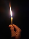 Close-up of hands holding a glowing candle in a dark room.