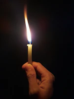 A close-up of hands gently holding a glowing energetic candle with warm golden light.