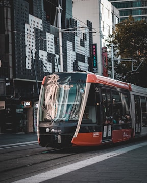 A modern tram travels on urban tracks with tall buildings and storefronts visible in the background. The tram is primarily black, red, and white and has a digital display indicating its destination as Circular Quay.