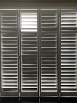 Vertical window blinds are evenly arranged, allowing faint light to pass through, creating a pattern of light and shadow.