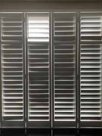 Vertical window blinds are evenly arranged, allowing faint light to pass through, creating a pattern of light and shadow.