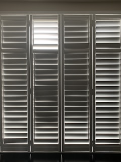 Vertical window blinds are evenly arranged, allowing faint light to pass through, creating a pattern of light and shadow.