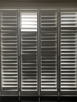 Vertical window blinds are evenly arranged, allowing faint light to pass through, creating a pattern of light and shadow.