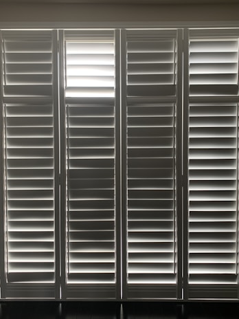 Vertical window blinds are evenly arranged, allowing faint light to pass through, creating a pattern of light and shadow.