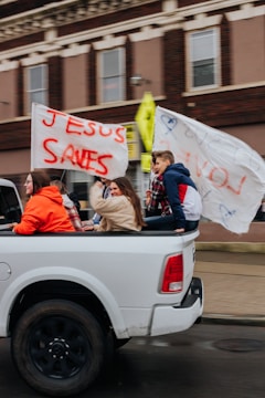 a group of people in a pickup truck with a banner of Jesus saying Jesus saves