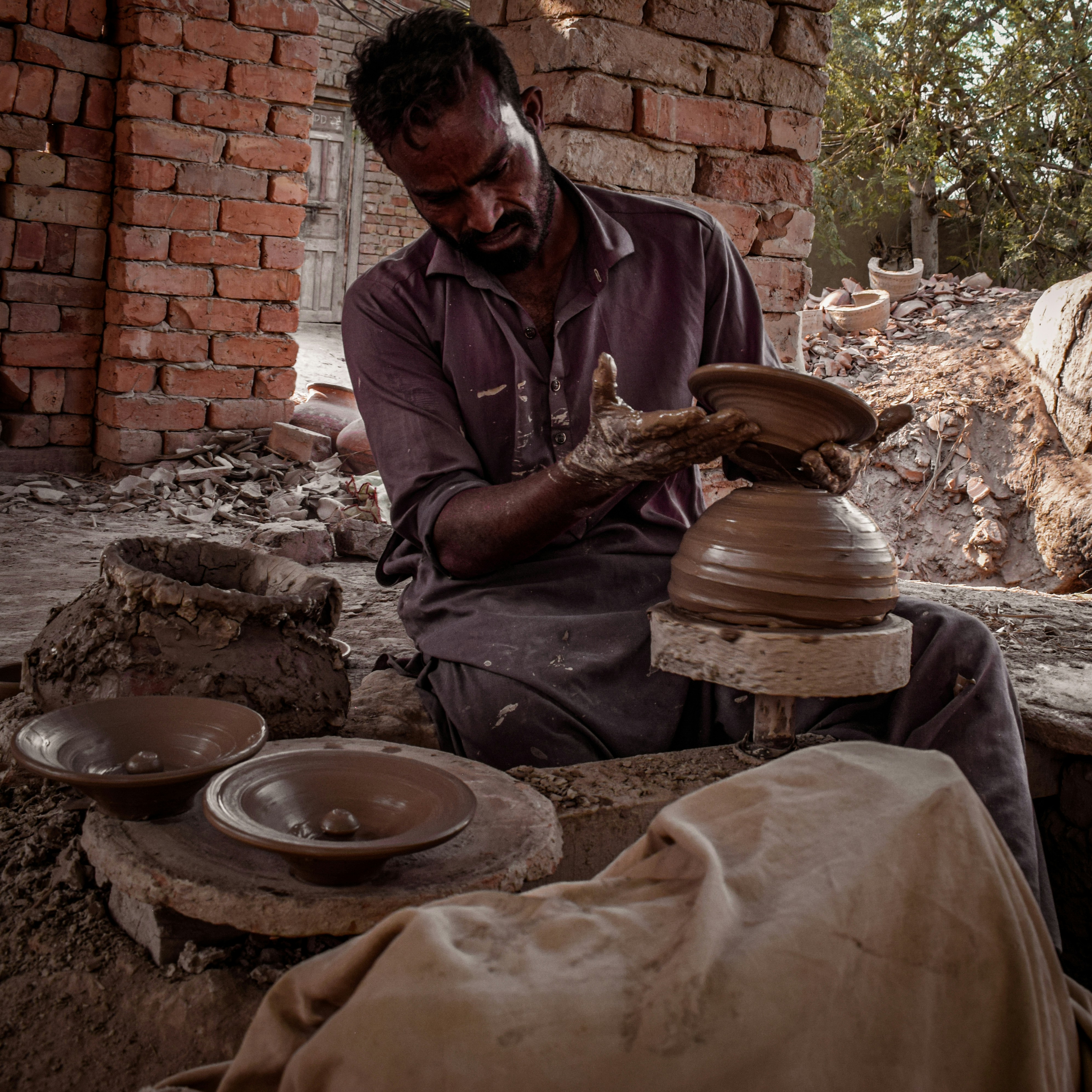 An artisan shaping a vibrant clay pot on a spinning wheel in a cozy studio filled with ceramic pieces.